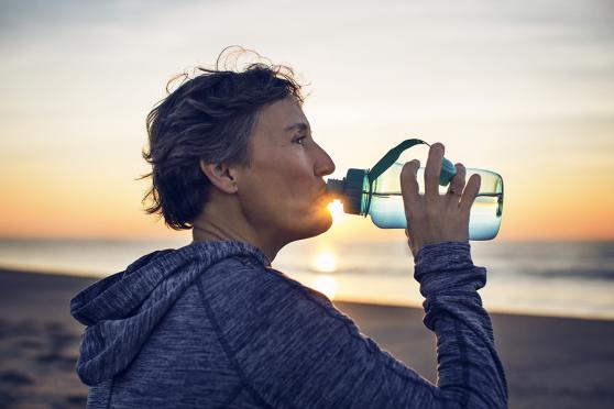 Woman outdoors drinking water from clear bottle